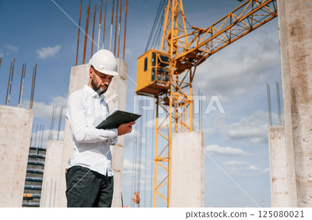 Inspector with notepad is standing on the construction site Inspector with notepad is standing on the construction site 125080021