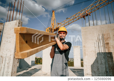 Holding and walking with wooden plank. Man in uniform is working on the construction site Holding and walking with wooden plank. Man in uniform is working on the construction site 125080096