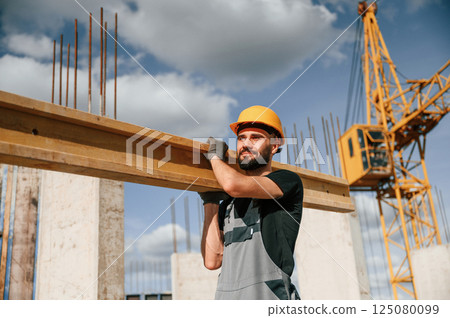 Holding and walking with wooden plank. Man in uniform is working on the construction site Holding and walking with wooden plank. Man in uniform is working on the construction site 125080099