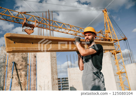 Front view of man that is in uniform holding wooden plank on the construction site 125080104