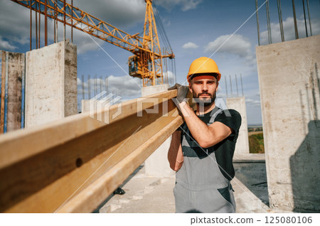 Wooden plank in hands. Man in uniform is working on the construction site 125080106