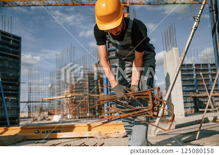 Working with rusty metal pieces. Man in uniform is on the construction site Working with rusty metal pieces. Man in uniform is on the construction site 125080158