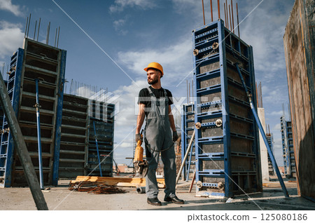 Standing with grinding machine in hands. Man in uniform is working on the construction site 125080186