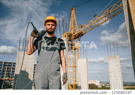 Portrait of man that is in uniform with the drill on the construction site 125080197