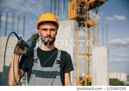 Portrait of man that is in uniform with the drill on the construction site Portrait of man that is in uniform with the drill on the construction site 125080198