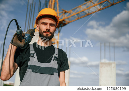Portrait of man that is in uniform with the drill on the construction site Portrait of man that is in uniform with the drill on the construction site 125080199