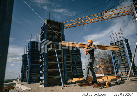 Yellow colored wooden plank. Man in uniform is working on the construction site 125080204