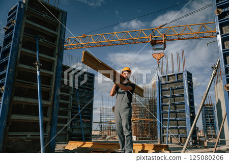 Yellow colored wooden plank. Man in uniform is working on the construction site Yellow colored wooden plank. Man in uniform is working on the construction site 125080206