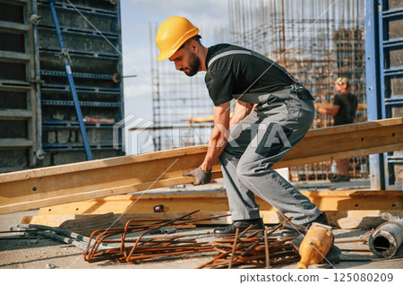 Placing wooden plank on the floor. Man in uniform is working on the construction site Placing wooden plank on the floor. Man in uniform is working on the construction site 125080209