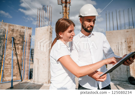 Reading the document in notepad. Man in uniform working with woman on the construction site Reading the document in notepad. Man in uniform working with woman on the construction site 125080234