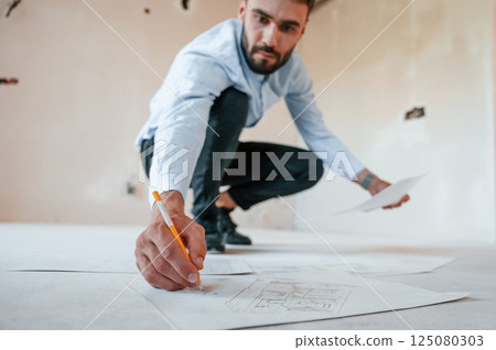 On the floor with project plan. The man is making repairs in the apartment On the floor with project plan. The man is making repairs in the apartment 125080303