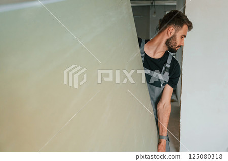 Moving big part of construction material by hands. The man is making repairs in the apartment Moving big part of construction material by hands. The man is making repairs in the apartment 125080318