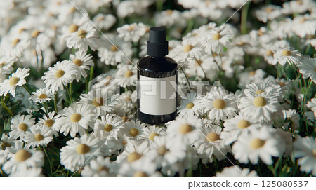 Chamomile flowers around a skincare bottle against a pure white backdrop.  125080537