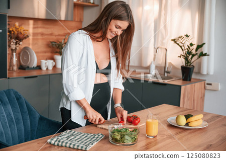 Preparing the salad on kitchen. Beautiful pregnant woman is indoors at home Preparing the salad on kitchen. Beautiful pregnant woman is indoors at home 125080823