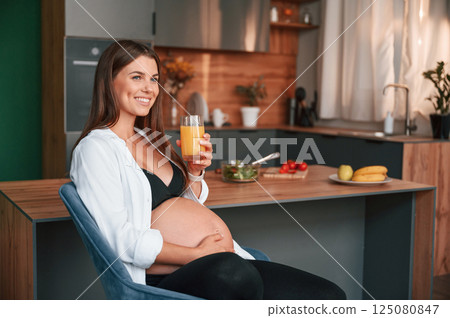 With orange juice. Beautiful pregnant woman is indoors at home With orange juice. Beautiful pregnant woman is indoors at home 125080847