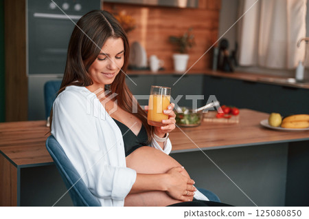 With orange juice. Beautiful pregnant woman is indoors at home With orange juice. Beautiful pregnant woman is indoors at home 125080850