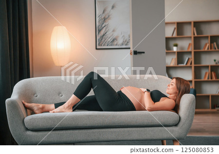Laying down on the sofa. Beautiful pregnant woman is indoors at home 125080853