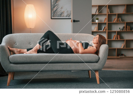 Laying down on the sofa. Beautiful pregnant woman is indoors at home Laying down on the sofa. Beautiful pregnant woman is indoors at home 125080856