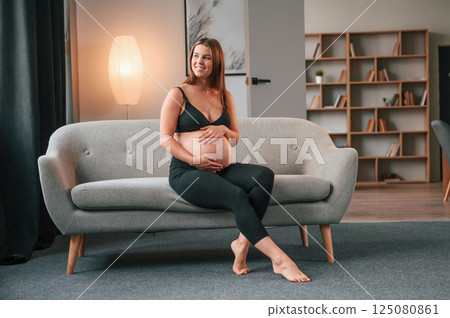 On the sofa. Beautiful pregnant woman is indoors at home 125080861