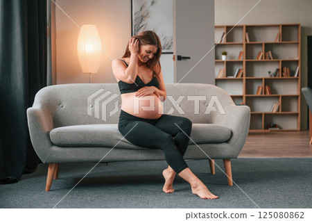 On the sofa. Beautiful pregnant woman is indoors at home 125080862