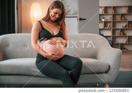On the sofa. Beautiful pregnant woman is indoors at home 125080863