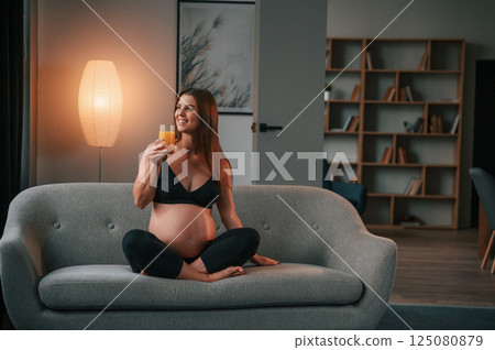 Sitting on the sofa and drinking orange juice. Beautiful pregnant woman is indoors at home Sitting on the sofa and drinking orange juice. Beautiful pregnant woman is indoors at home 125080879