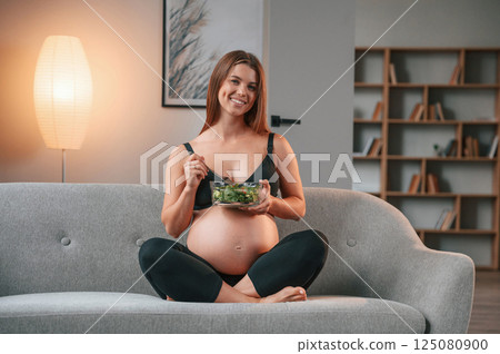 Conception of diet. Eating salad. Beautiful pregnant woman is indoors at home Conception of diet. Eating salad. Beautiful pregnant woman is indoors at home 125080900