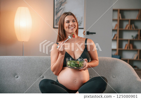 Conception of diet. Eating salad. Beautiful pregnant woman is indoors at home Conception of diet. Eating salad. Beautiful pregnant woman is indoors at home 125080901