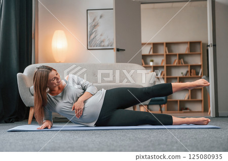 Doing yoga exercises. Beautiful pregnant woman is indoors at home Doing yoga exercises. Beautiful pregnant woman is indoors at home 125080935
