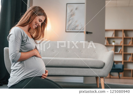 Side view. Sitting on the floor. Beautiful pregnant woman is indoors at home Side view. Sitting on the floor. Beautiful pregnant woman is indoors at home 125080940