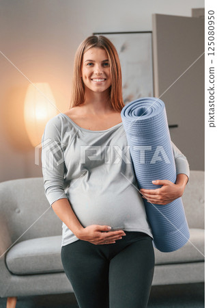 Blue colored yoga mat is in hand. Beautiful pregnant woman is indoors at home 125080950