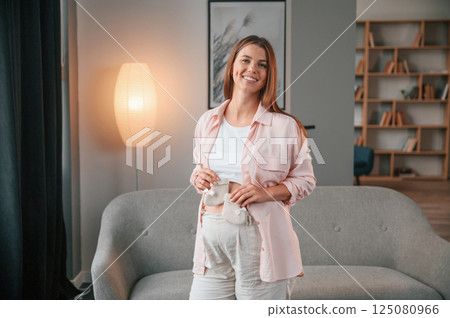 Holding cute little socks. Beautiful pregnant woman is indoors at home Holding cute little socks. Beautiful pregnant woman is indoors at home 125080966