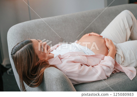 Resting on the sofa. Beautiful pregnant woman is indoors at home 125080983
