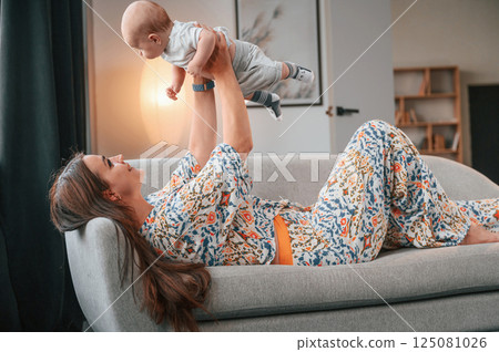 Laying down on the sofa. Beautiful happy mother with her newborn son is at home Laying down on the sofa. Beautiful happy mother with her newborn son is at home 125081026