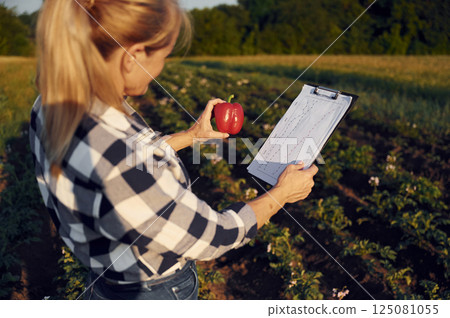 Pepper and notepad with information in hands. Woman is on the agricultural field at daytime 125081055