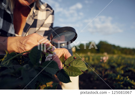Using magnifying glass. Woman is on the agricultural field at daytime 125081067