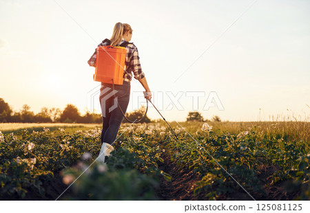 Rear view of woman that using equipment for sprinkle potato on the agricultural field at daytime 125081125