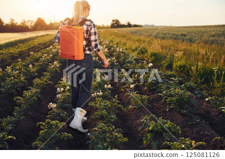 Rear view of woman that using equipment for sprinkle potato on the agricultural field at daytime 125081126