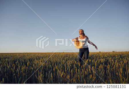 With straw hat. Feeling good. Positive emotions. Concept of freedom. Woman is on the agricultural field at daytime With straw hat. Feeling good. Positive emotions. Concept of freedom. Woman is on the agricultural field at daytime 125081131