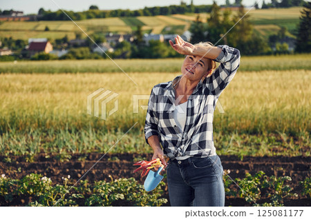 Standing and holding little showel and other garden tools. Woman is on the agricultural field at daytime Standing and holding little showel and other garden tools. Woman is on the agricultural field at daytime 125081177