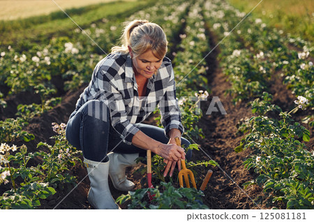 Sitting and working by using garden tools. Woman is on the agricultural field at daytime 125081181