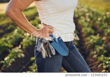 Close up view. With gloves and little showel. Woman is on the agricultural field at daytime 125081231