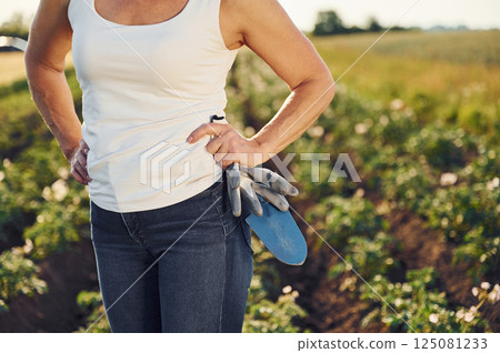 Close up view. With gloves and little showel. Woman is on the agricultural field at daytime Close up view. With gloves and little showel. Woman is on the agricultural field at daytime 125081233