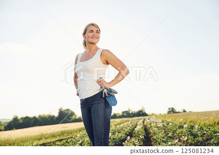 Standing in sunlight and smiling. Woman is on the agricultural field at daytime Standing in sunlight and smiling. Woman is on the agricultural field at daytime 125081234