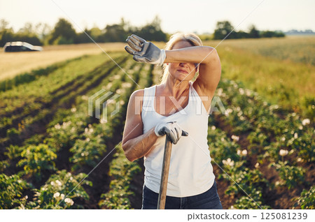 Tired of work. With showel. Woman is on the agricultural field at daytime 125081239