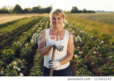 With showel in hands. Woman is on the agricultural field at daytime With showel in hands. Woman is on the agricultural field at daytime 125081242