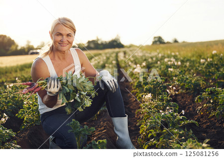 Sitting and holding beetroot in hand. Woman is on the agricultural field at daytime Sitting and holding beetroot in hand. Woman is on the agricultural field at daytime 125081256