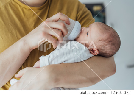 Close up father carrying and feeding his newborn baby with formula milk bottle. Food Adoption. Child health and skin care concept. Problems with breastfeeding, food allergy, gassy stomach, colics 125081381