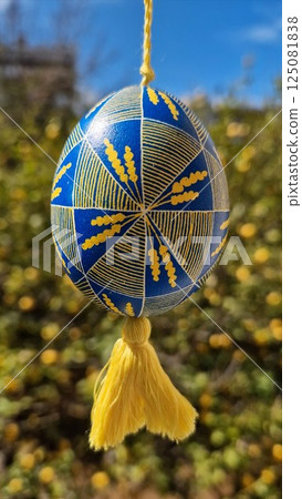 Colorful Ukrainian pysanka featuring traditional patterns in national colors yellow blue, showcasing intricate design and vibrant Easter eggs hung against a beautiful natural background 125081838