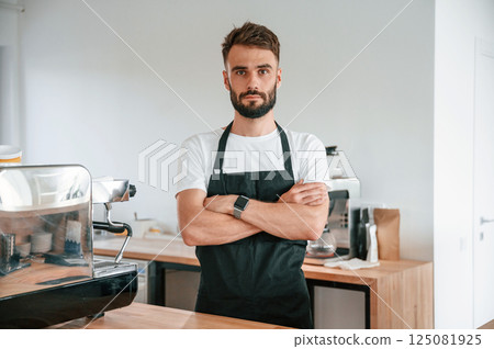 Standing with arms crossed. Cafe worker in white shirt and black apron is indoors 125081925